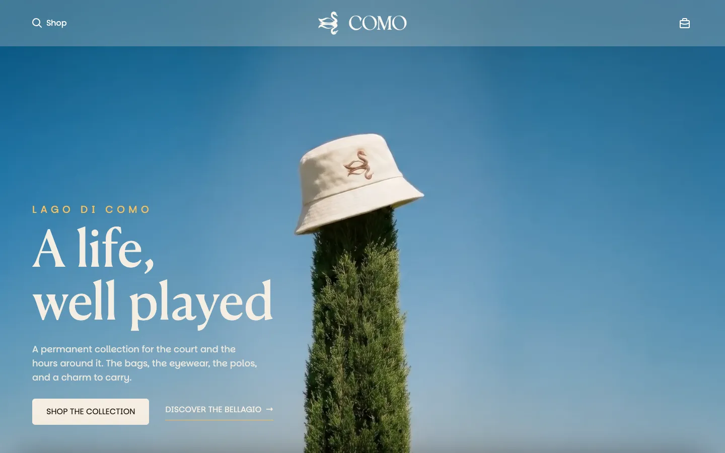 COMO homepage, a bucket hat resting on a cypress against a blue sky